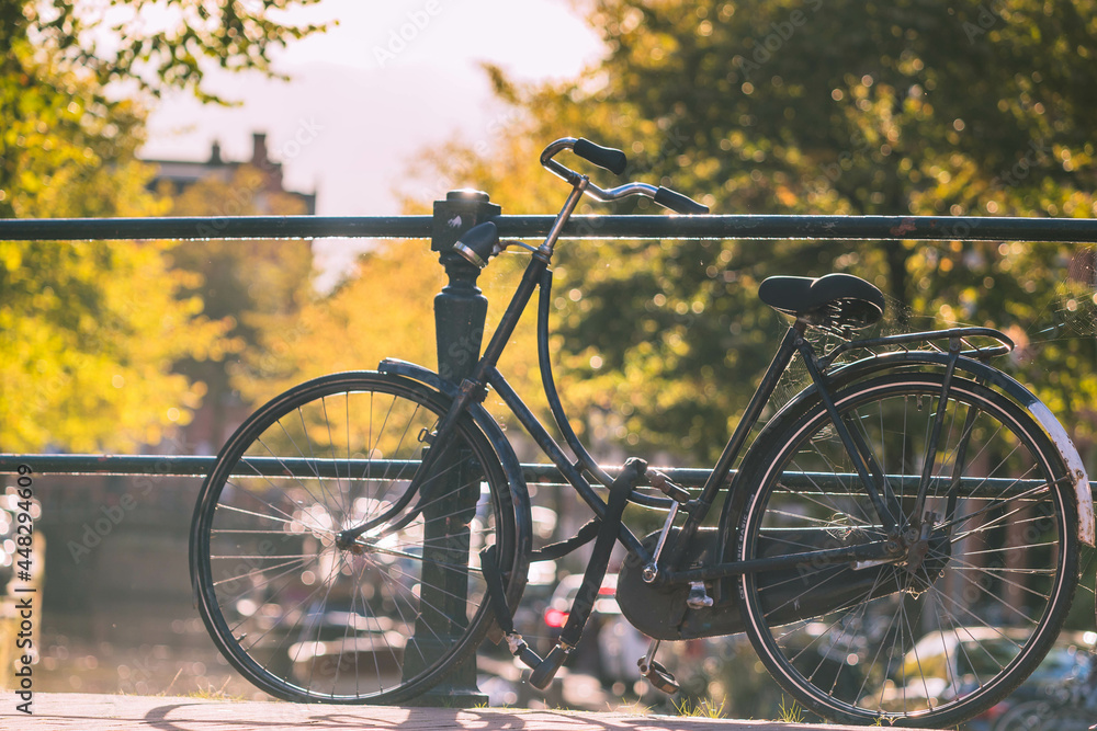 Fototapeta premium Vintage classic bicycle parked on a canal bridge in Amsterdam with soft sunlight in evening, Netherlands land of bicycle, Cycling is a common mode of transport in the Holland.