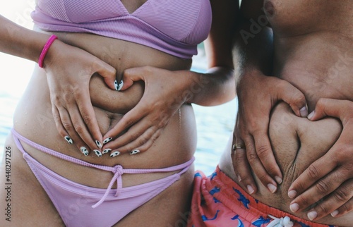 Image of body sizes and shapes , two friends holding heart hands around belly button 