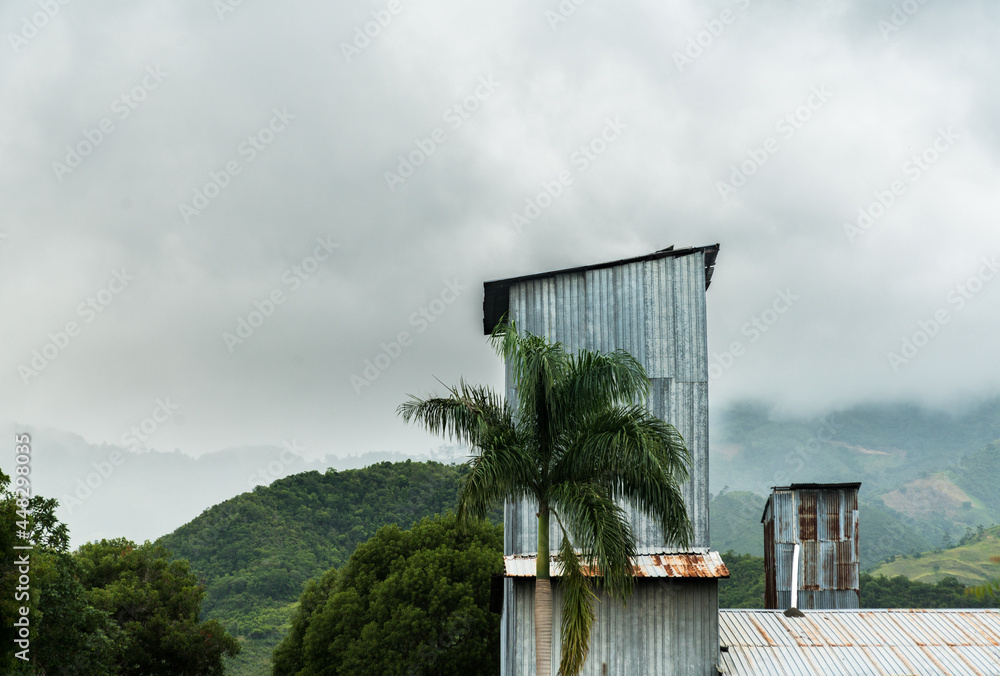 Dramatic image of a coffee plantation metal storage buildings high in the Caribbean mountains of the Dominican Republic, with foggy cloudy skies.