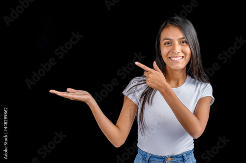 Canvas Print Beautiful Latin woman with white t-shirt on black background with her outstretched hand holding imaginary and the other hand pointing to the imaginary held item
