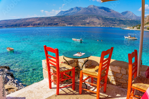 Scenic view with tables and wooden chairs by the sea at the picturesque seaside village Limeni. Traditional houses and colorful stoned buildings in Limeni  Mani area  Laconia  Greece