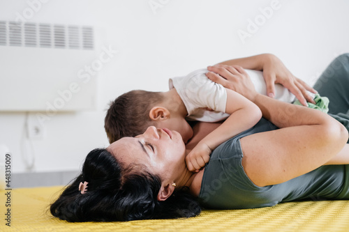Mother playing with cute disabled child. Talking and communicating with cerebral palsy boy on the floor, mat, doing exercises at home. Woman laughing with kid, physical or mental limits in movements
