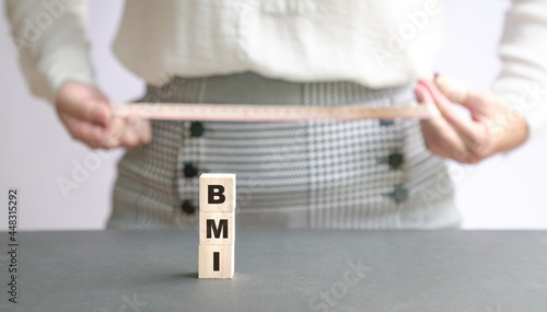 BMI word on wood cubes with woman measuring waist hip with a tape at the background. Copy space.