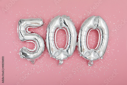 From above of silver shiny balloons demonstrating number 500 on pink background with scattered glitter