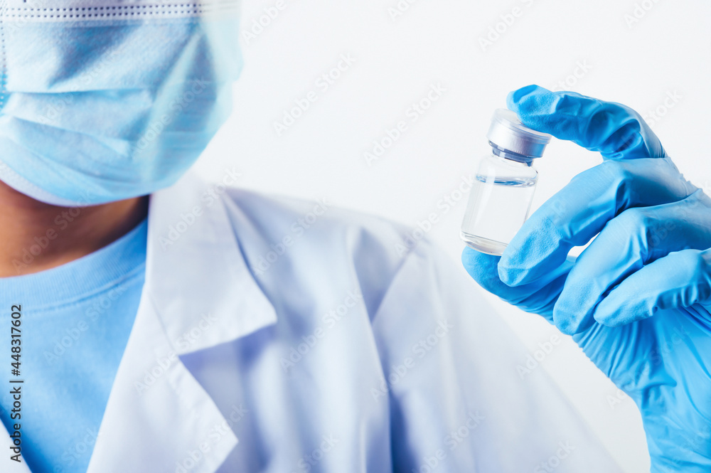 Closeup vial of covid-19 vaccine in hand of professional scientist or doctor in laboratory for treatment with mask gloves and lab coat on white background. Health business and industry concept. Closeup vial of covid-19 vaccine in hand of professional scientist or doctor in laboratory for treatment with mask gloves and lab coat on white background. Health business and industry concept.