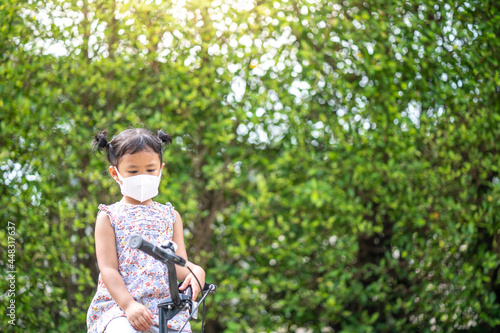 Cute small girl with protective face mask on bicycle outdoor.