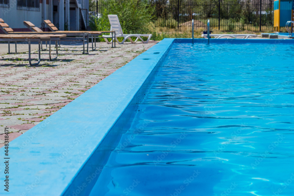 Outdoor swimming pool with a clear blue water. Steel railings stairs and sun loungers.