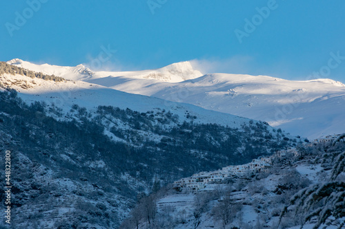 Poqueira ravine with Capileira looming over the edge of the mountain and the Veleta peak in the Sierra Nevada in the background, all white from a snowfall.