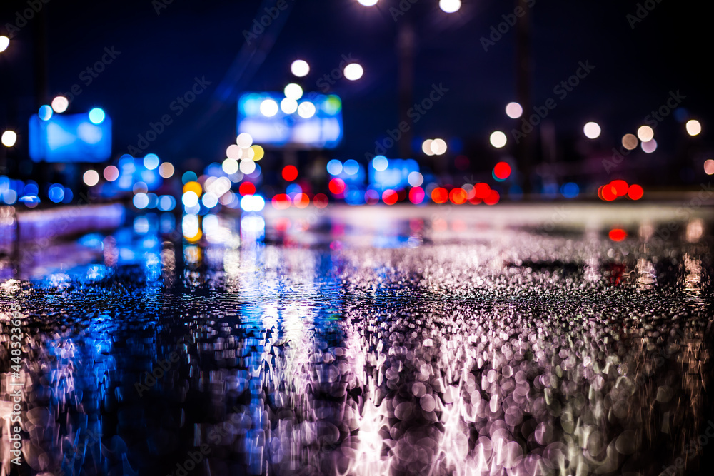 Rainy night in the big city, the light from the headlamps of vehicles approaching on the highway. View from the level of asphalt