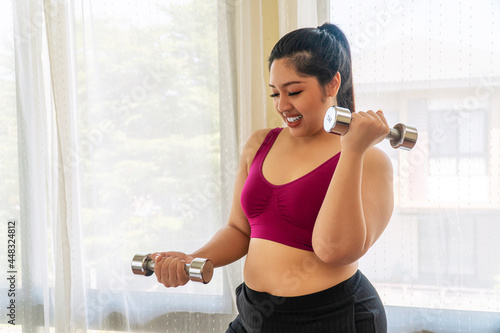 Activity exercise fit body for diet or obesity concept. Positive happy overweight fat woman holding dumbbells in own hands workout dieting weight loss while standing in the room. photo