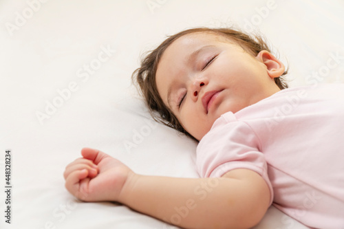 Fotografia, Obraz Little baby girl 12 months wearing pink cloth sleeping on white bed at home