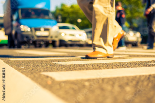 Sunny day in a city, pedestrians crossing the road. View from the level of asphalt