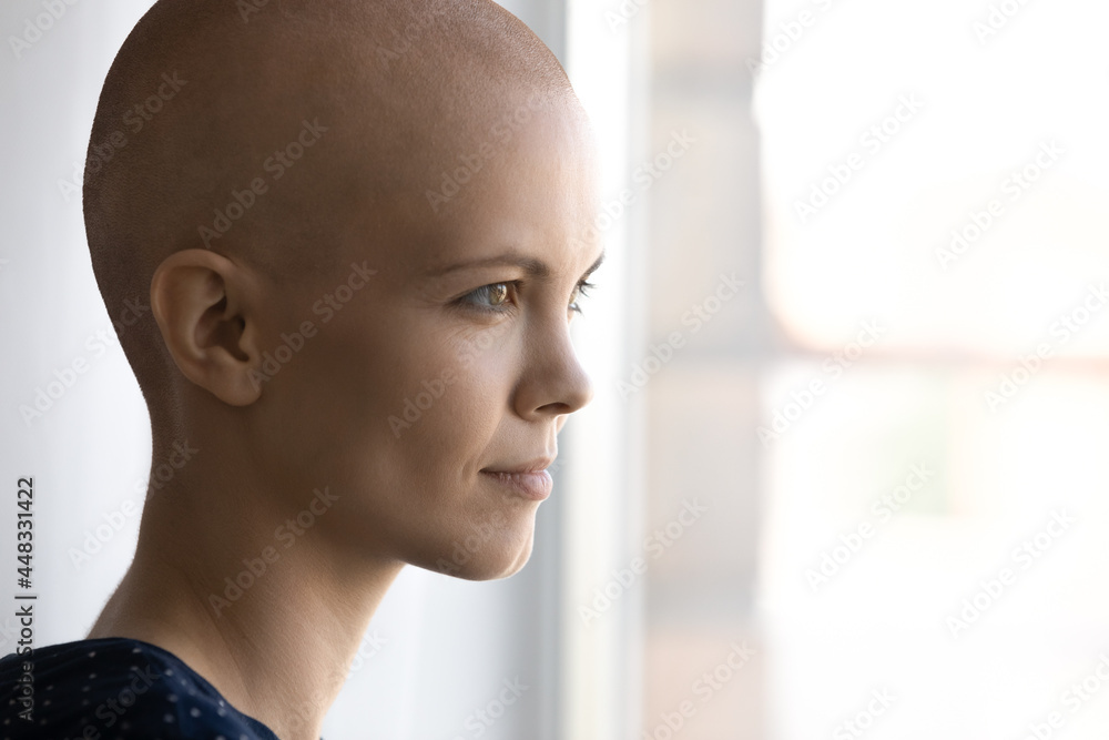 Side head shot close up view smiling hairless after chemotherapy pensive woman looking out of window, visualizing healthy future or effective cancer treatment, feeling hopeful indoors, copy space. Side head shot close up view smiling hairless after chemotherapy pensive woman looking out of window, visualizing healthy future or effective cancer treatment, feeling hopeful indoors, copy space.