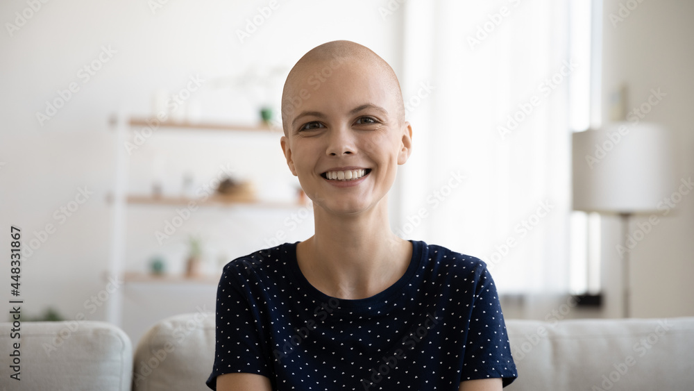 Head shot portrait of happy young bald after chemotherapy woman looking at camera. Smiling sincere millennial hairless lady holding video call with doctor, feeling excited of hearing positive news.
