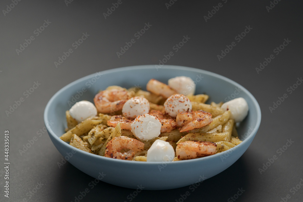 Penne pasta with shrimps and mozzarella and pesto in blue bowl Penne pasta with shrimps and mozzarella and pesto in blue bowl