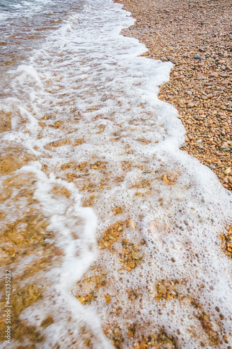 in motion wave of clear sea water with foam rolls onto rocky shore. vertical travel content, selective focus