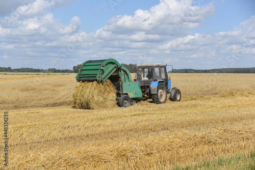 The tractor collects straw in large bales in the field.