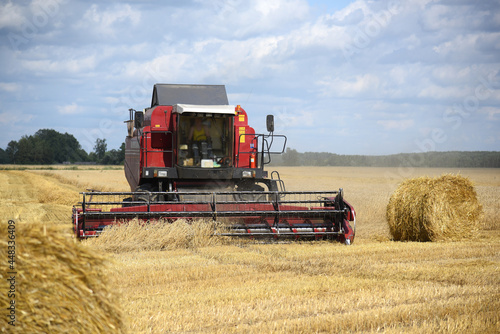 A grain harvester collects ripe ears of grain  there are bales of straw on the field.