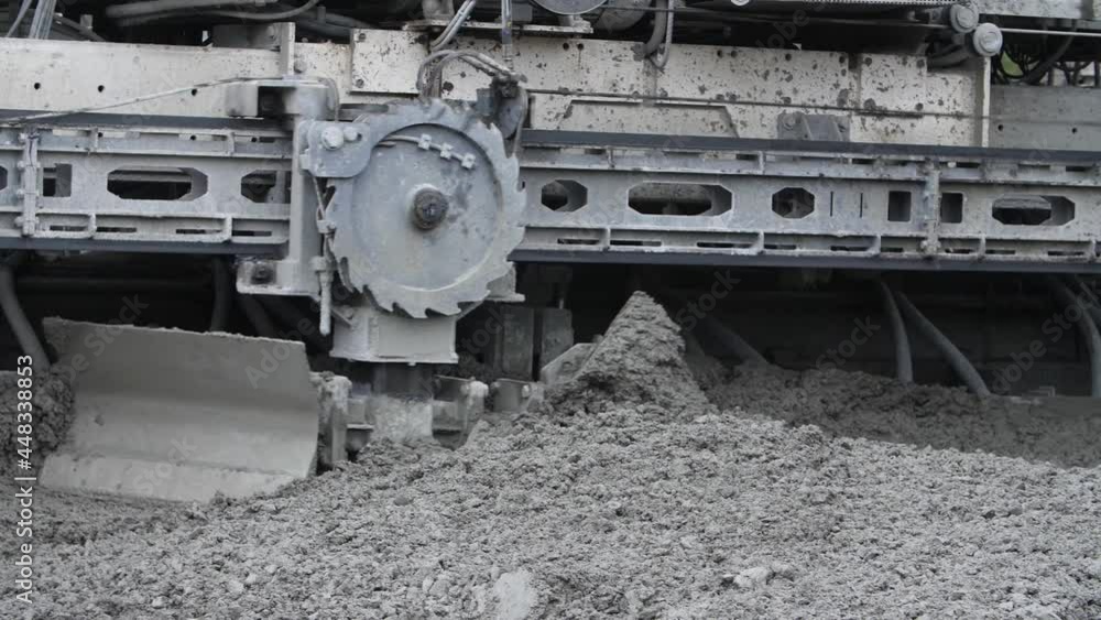 Moving part of slipform paver or heavy road construction machine spreading concrete material mass over motorway surface. Concept of automatic mechanical operation of highway or roadway paving process. Moving part of slipform paver or heavy road construction machine spreading concrete material mass over motorway surface. Concept of automatic mechanical operation of highway or roadway paving process.