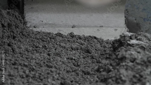 Close-up view of asphalt or concrete material mass moved by paver, spreader or road paving machine. Concept of roadwork operation with substance for roadbed construction, highway paving process.