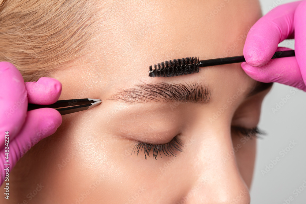 Makeup artist combs  and plucks eyebrows after dyeing in a beauty salon.Professional makeup and cosmetology skin care.
