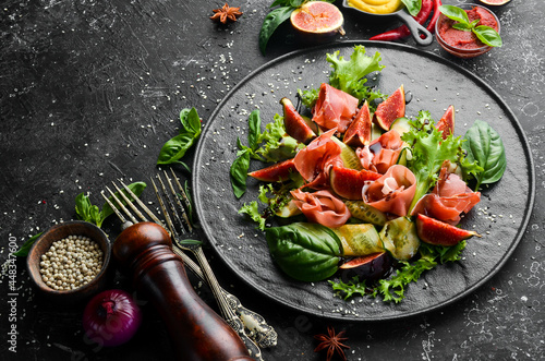 Green salad with prosciutto, cucumber and fig on a black stone plate. Food. Top view. Free space for your text.