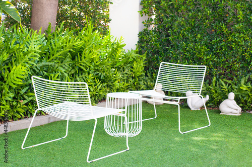 White chair and small table set in green garden, tea table set for relaxation at home garden.