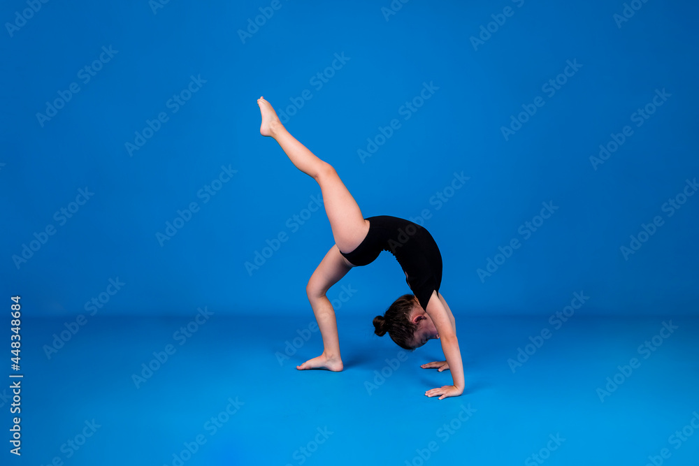 a small gymnast in a black swimsuit stands on her hands on a blue background with a place for text a small gymnast in a black swimsuit stands on her hands on a blue background with a place for text