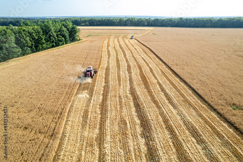 A combine harvester in the field is harvesting grain and a truck is approaching it to load grain. Aerial view.