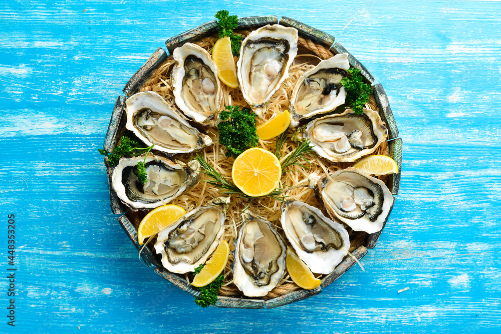 Open oysters in a wooden box on a blue wooden background. Free space for text. Top view. Flat lay. Open oysters in a wooden box on a blue wooden background. Free space for text. Top view. Flat lay.