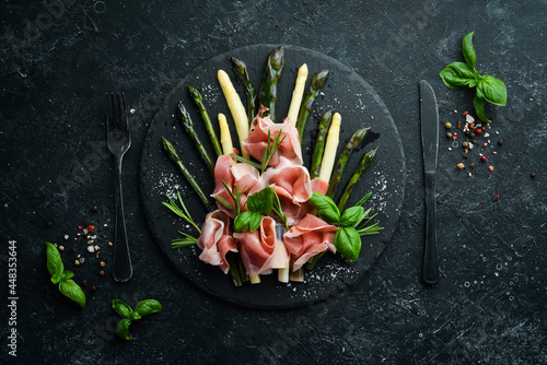 Prosciutto with boiled asparagus and spices on a black stone plate. Top view. Free space for your text.