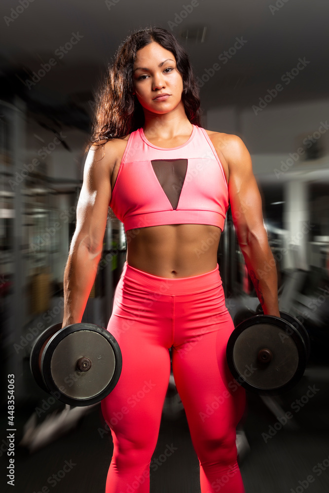 portrait of young hispanic female bodybuilder with dumbbells at gym portrait of young hispanic female bodybuilder with dumbbells at gym