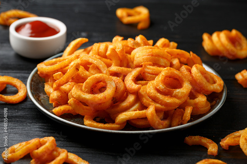 Golden Curly Fries with ketchup on rustic plate photo