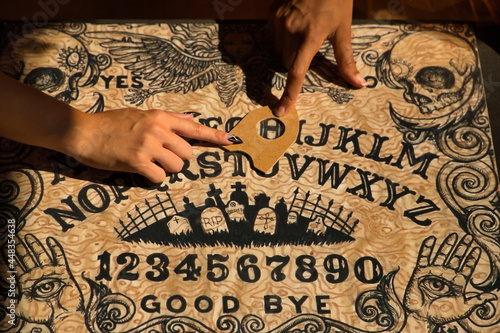 Detail of young hispanic and latin women's hands on a ouija board pointing to the letter h. photo