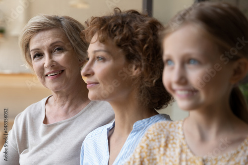 Head shot portrait close up of smiling beautiful mature woman posing with adult daughter and adorable little granddaughter, happy three generations of women standing in row, growing process
