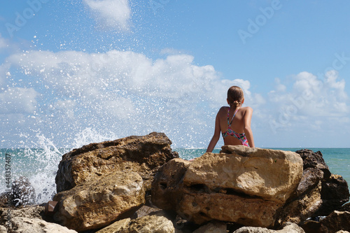 girl sitting on a large stone on the shore and dreamily looking at the sea back view