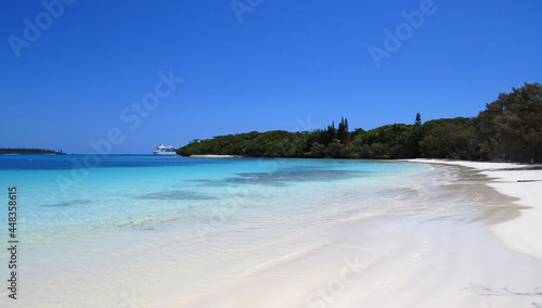 Turquoise water white sandy beach with a cruise ship docking on the background in Isle of Pines, New Caledonia.