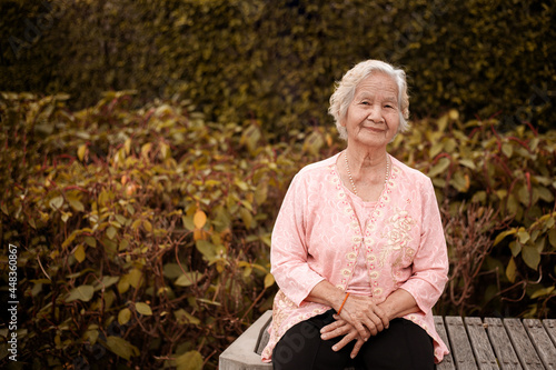 Smile Asian senior woman sitting on a wooden chair in the  garden, eldery woman.
