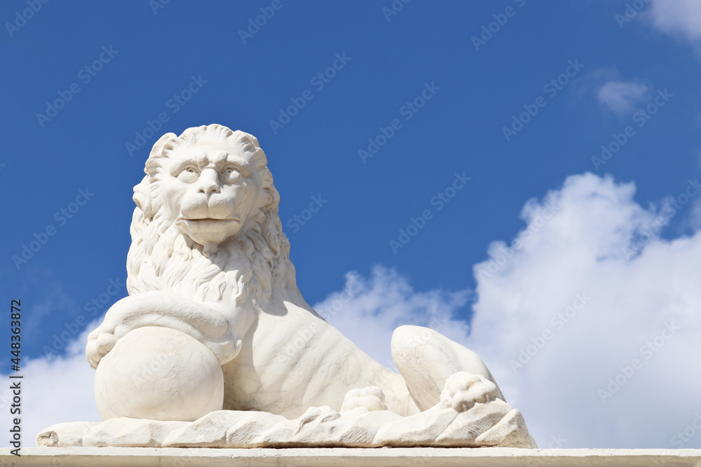 Stone lion with sphere decorating park in Museum-Estate of Arkhangelskoye near the Moscow. Marble sculpture on blue sky with white clouds background, work of an unknown sculptor of 18th century