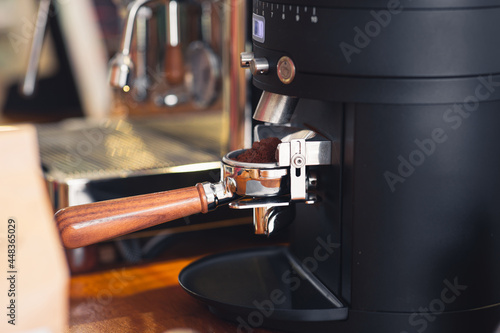 Coffee portafilter engaged bean grinder, close up detail view copy space includes.