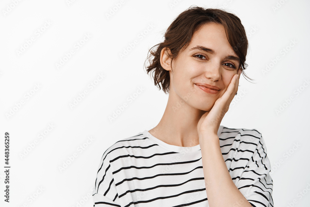 Close up portrait of beautiful young woman smiling, touching healthy clean skin, skincare cosmetics advertisement, standing over white background Close up portrait of beautiful young woman smiling, touching healthy clean skin, skincare cosmetics advertisement, standing over white background