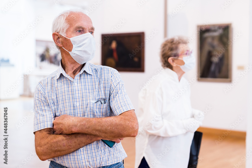 Obraz premium mature man in mask protecting against covid examines paintings on display in hall of art museum