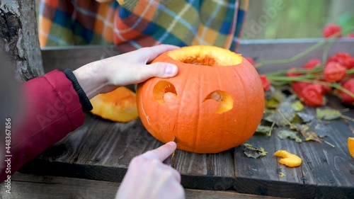 Family preparing halloween pumpkin. Hands carves a scary halloween pumpkin on a wooden bench in the garden. Making pumpkin decor for Halloween. Preparation for celebration.