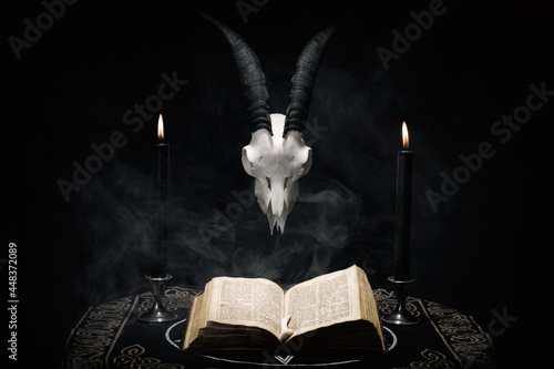 Open old book, goat skull and  black candles on witch table. Occult, esoteric, divination and wicca concept. Halloween background.
 photo