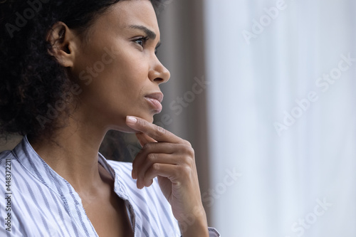 Close up of unhappy pensive young African American woman look in window distance thinking pondering. Thoughtful mixed race ethnicity female feel lonely lack communication on covid-19 lockdown at home.