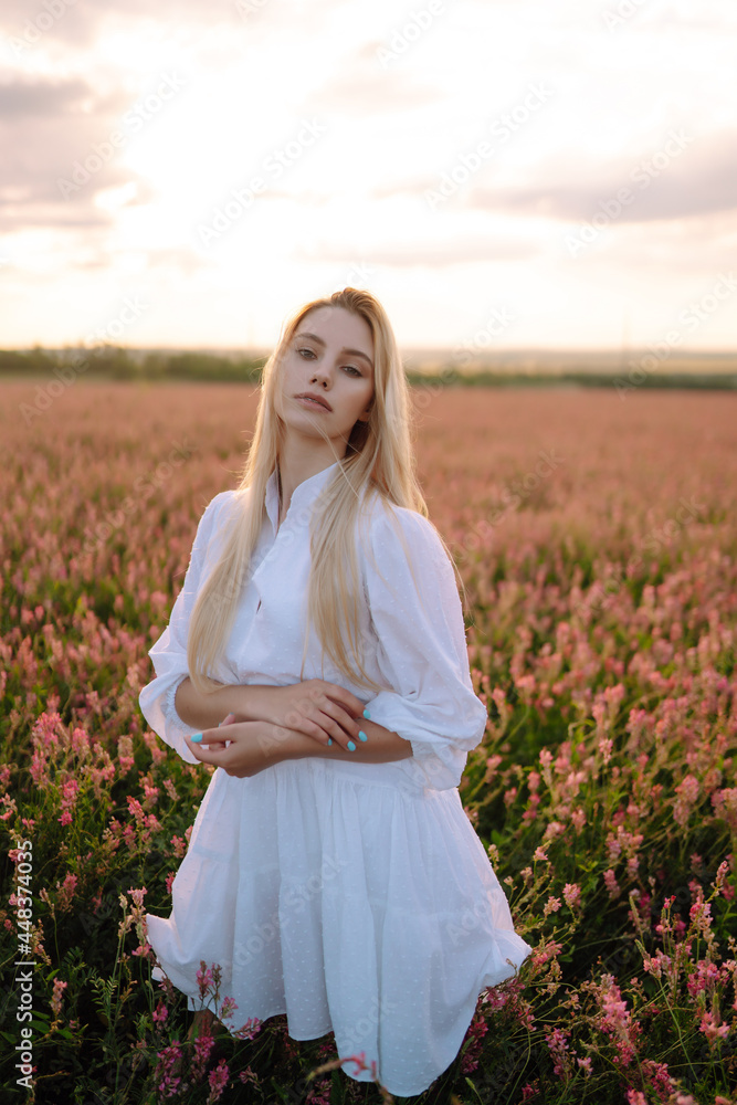 Beauty romantic girl Outdoors at sunset. Young woman in stylish clothes posing in the blooming field. Nature, vacation, relax and lifestyle. Fashion concept.