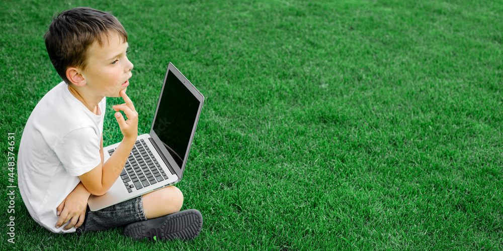 child sits on the grass and studies with a laptop online, enjoying nature child sits on the grass and studies with a laptop online, enjoying nature