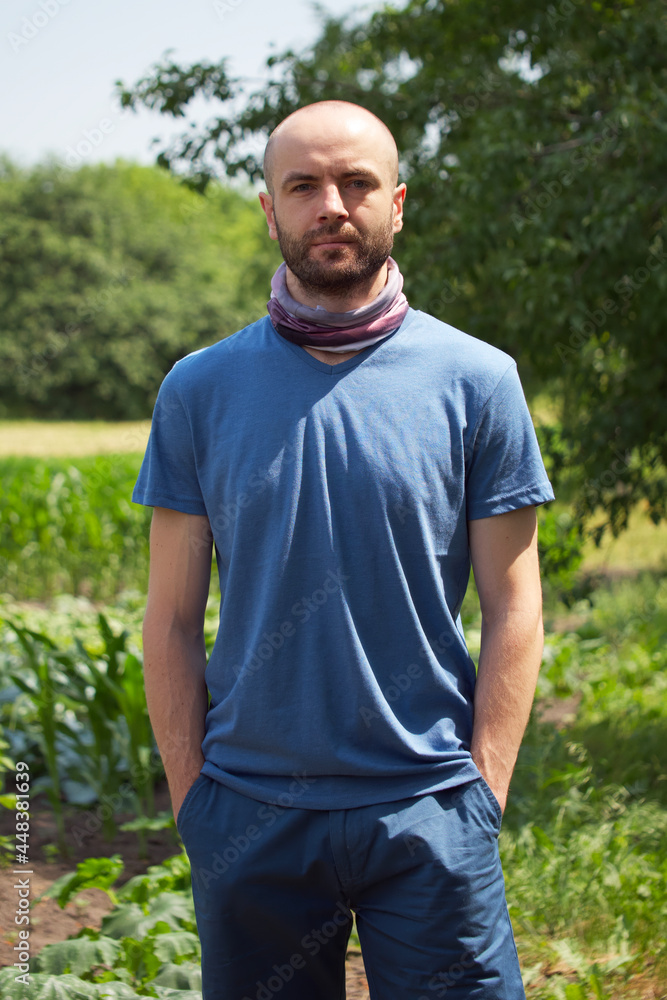 White man in a blue T-shirt and shorts. A bald man with stubble on his face holds his hands in his pockets. Looking into the camera. White man in a blue T-shirt and shorts. A bald man with stubble on his face holds his hands in his pockets. Looking into the camera.