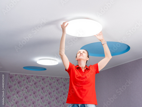 A woman in a children's room sets a ceiling lamp.