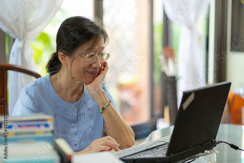 senior asian woamn using computer to send email to friend at home